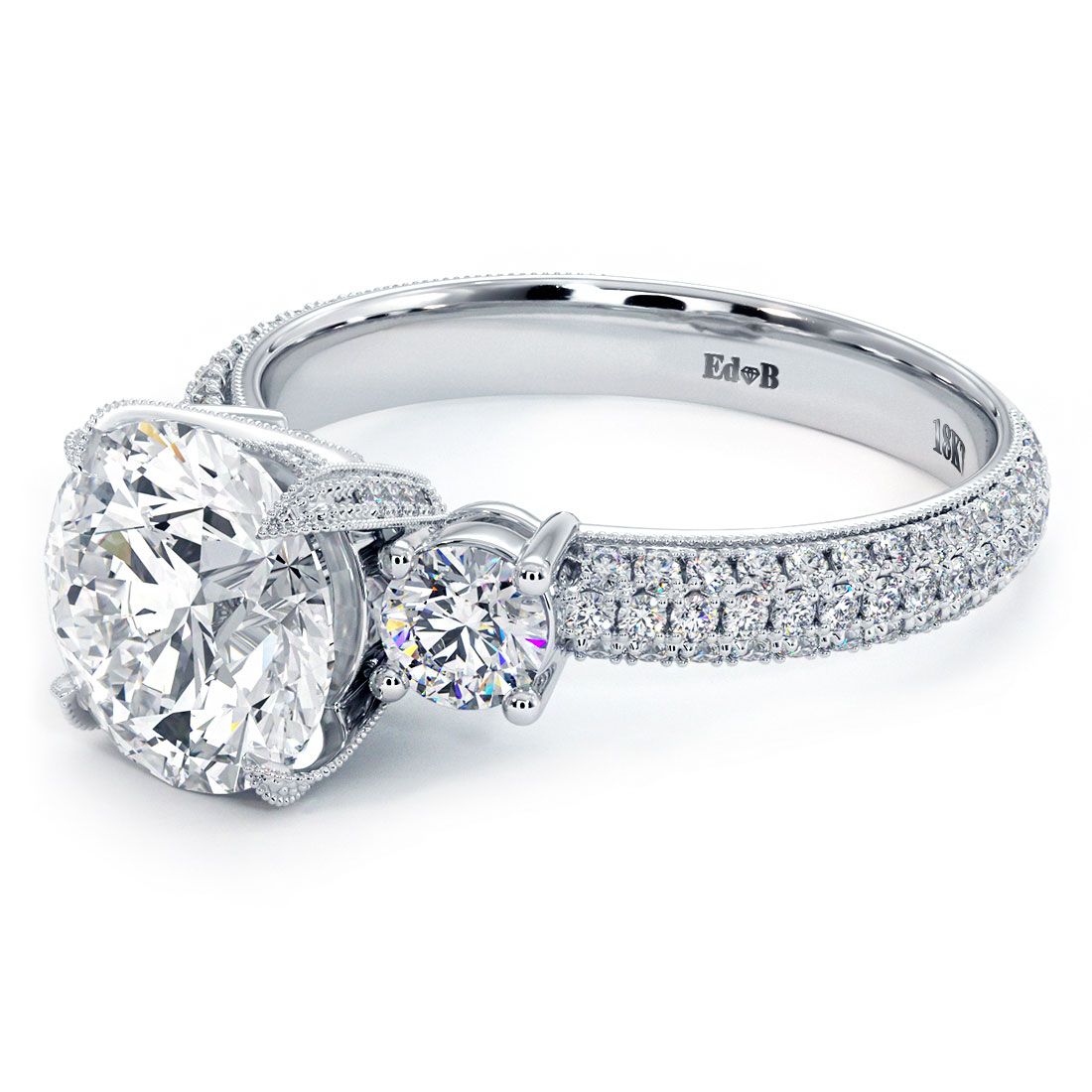 Angled display of a round diamond three-stone engagement ring in 18k white gold with pavé-set shank, emphasizing fire and sparkle – Find it at @globalskydiamonds | #DiamondDistrictNYC